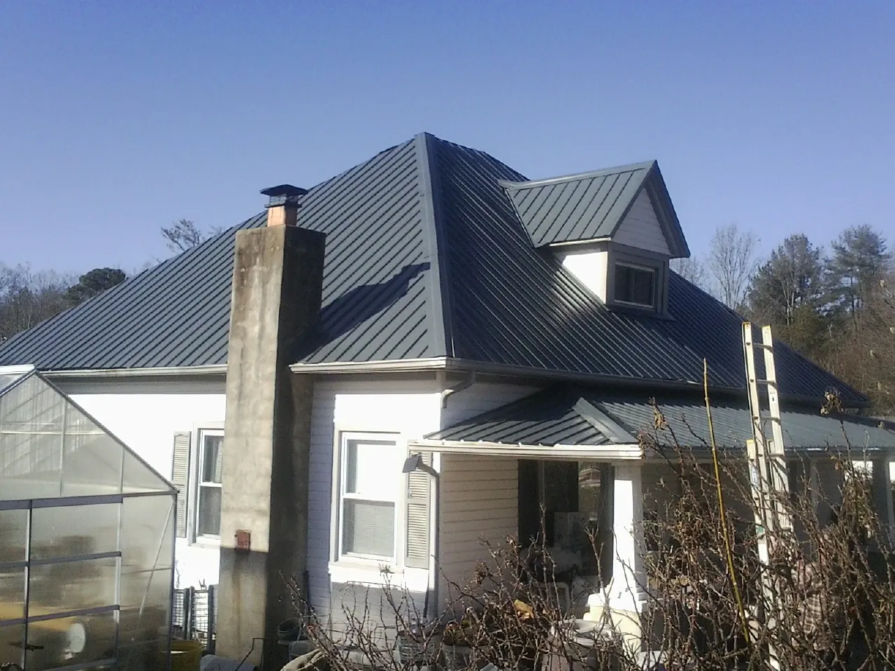 Dark blue standing seam metal roof on a white farmhouse with dormer — Slate & Tile Roof Repair by Roofing Brothers in Castle Rock