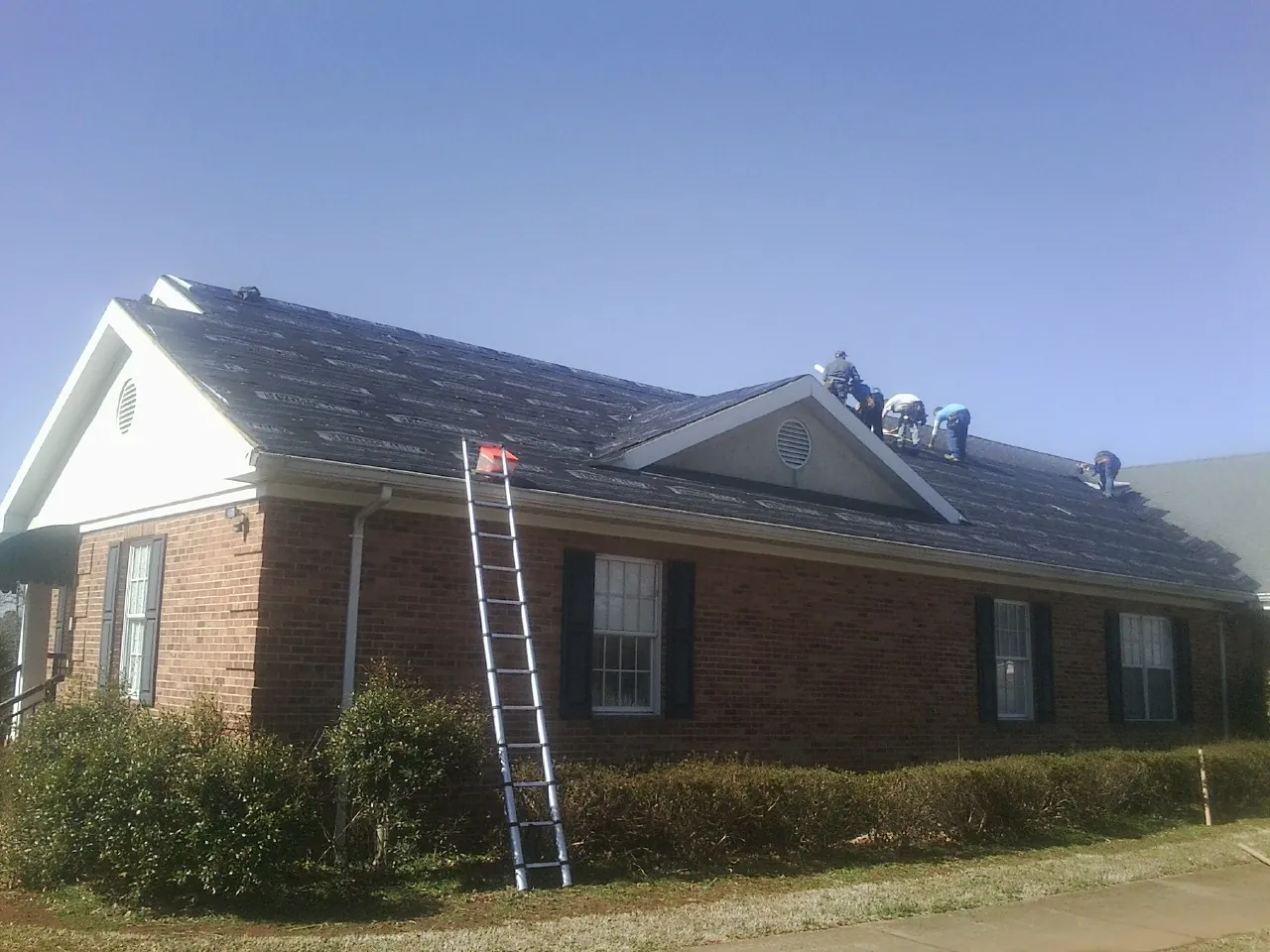 Crew tearing shingles off a brick ranch roof with a ladder set — Emergency Roof Repair work by our crew in Castle Rock