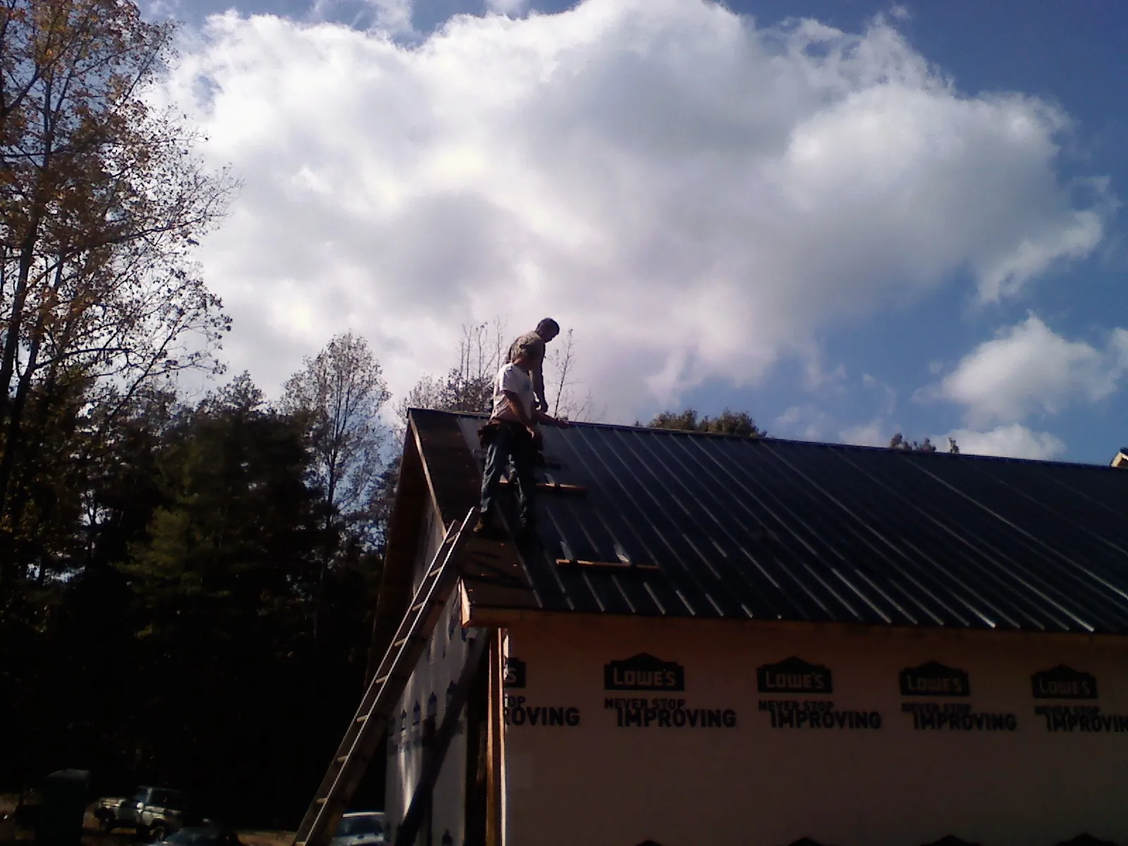 Roofer fastening dark metal panels high against a cloudy sky, from a Roof Inspection job in Castle Rock