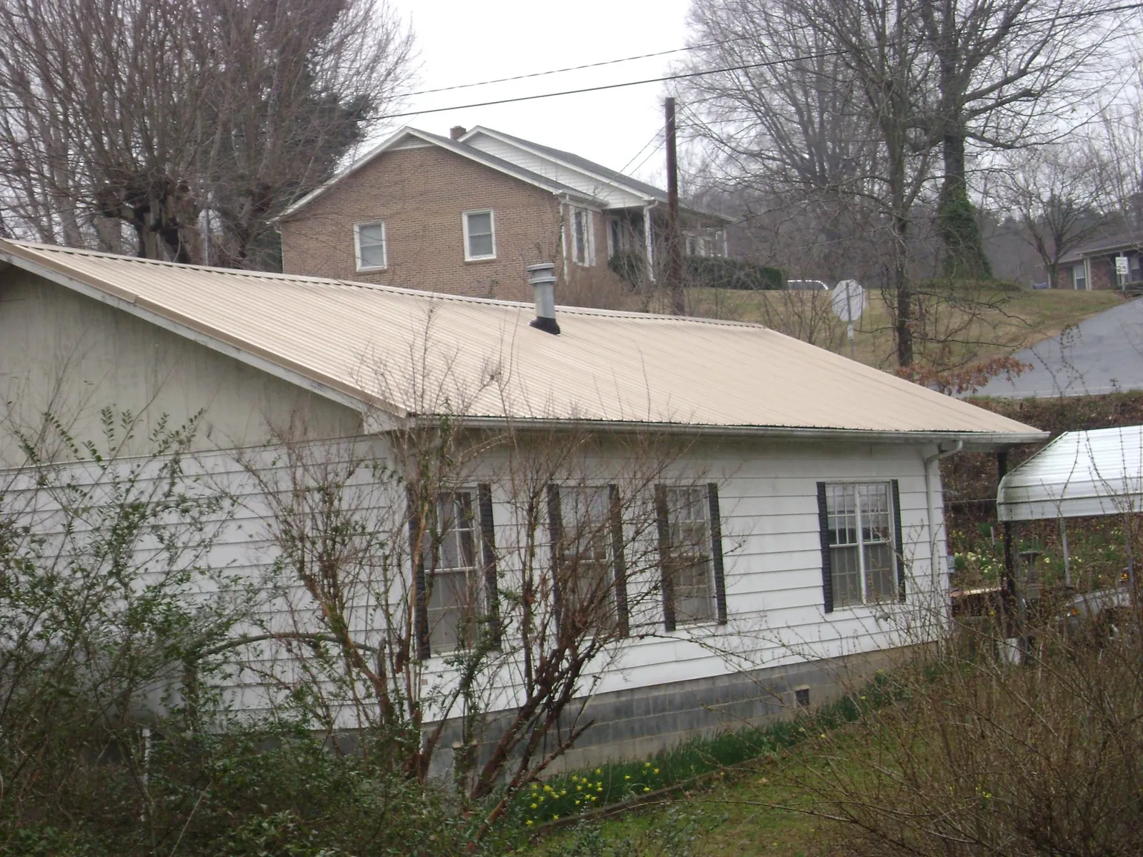 Tan metal roof on a white sided house set into a hillside — Commercial Roofing by Roofing Brothers in Castle Rock